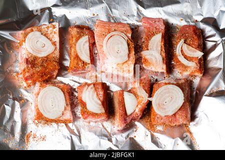 Rohe Schweineribs mit rohen Zwiebeln liegen auf Folie, fertig zum Backen im Ofen. Stockfoto