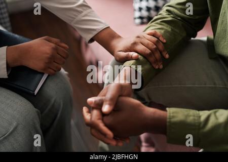 Junge afroamerikanische Psychologin, die die Hand des männlichen Patienten vor sich sitzend hält und seine Probleme teilt Stockfoto