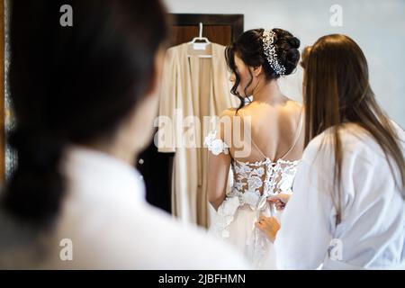 Brautjungfern helfen der Braut, ihr Kleid anzuziehen. Stockfoto