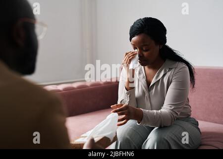 Junge gestresste weibliche Patientin nahm ein Taschentuch, um Tränen abzuwischen, während sie ihre Probleme der Psychoanalytikerin während der Sitzung beschrieb Stockfoto