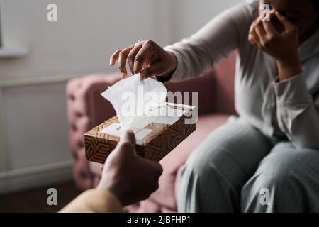 Hand einer jungen afroamerikanischen Patientin, die während der Sitzung ein Papiertaschentuch aus dem Karton nahm, das von einem Psychoanalytiker gehalten wurde Stockfoto