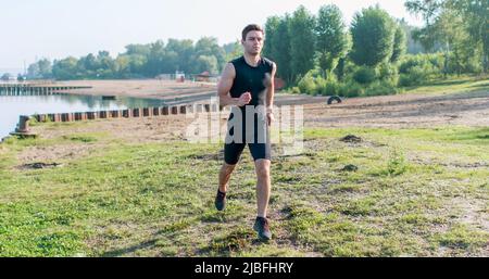 Porträt eines fitgen Sportlers beim Joggen auf der Straße am morgendlichen Sommertag. Outdoor-Training an der frischen Luft Stockfoto