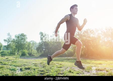 Porträt eines fitgen Sportlers beim Joggen auf der Straße am morgendlichen Sommertag. Outdoor-Training an der frischen Luft Stockfoto