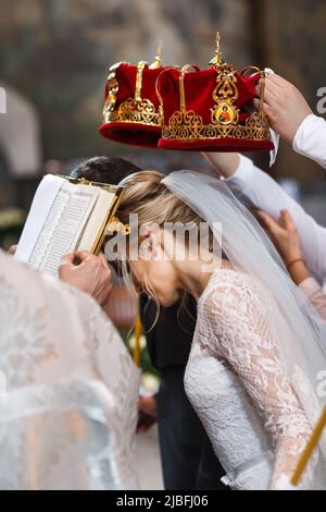 Zeugen der Braut und des Bräutigams halten bei einer Zeremonie in der Kirche Kronen Stockfoto