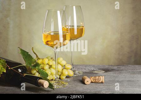 Weißwein in Gläsern, Weinflasche und Trauben auf einem alten Holztisch. Dunkler Hintergrund. Stockfoto