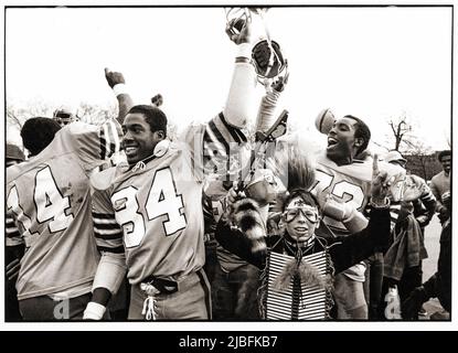 Die Fußballmannschaft der Canarsie High School und ihr Maskottchen feiern einen Sieg nach einem Spiel in Brooklyn, New York im Jahr 1982. Stockfoto