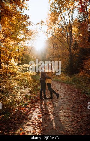 Ganzkörper-Seitenansicht eines glücklichen jungen Paares, das umarmt steht und sich im Herbstwald im Nationalpark in kanada anschaut Stockfoto