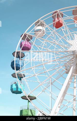 Von unten weißes Riesenrad mit bunten Karren gegen wolkenlosen blauen Himmel im Vergnügungspark Stockfoto