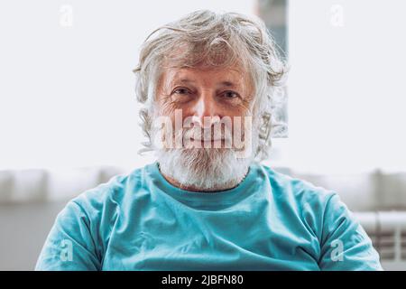 Älterer Mann mit grauem Bart vor verschwommenem Hintergrund und Blick auf die Kamera zu Hause Stockfoto