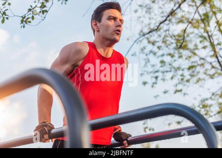 Fit Mann macht Trizeps Dips auf parallelen Bars im Park Training im Freien. Stockfoto