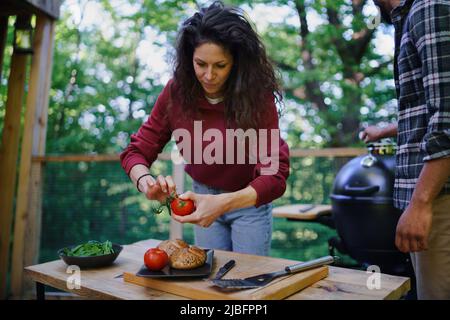 Glückliches Biracial Paar ruht sich aus und bereitet Burger im Freien in einem Baumhaus, Wochenende weg Stockfoto
