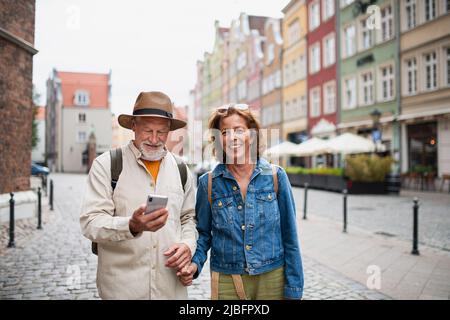 Porträt von glücklichen älteren Paar Touristen lächeln, halten die Hände, mit dem Smartphone im Freien in der historischen Stadt Stockfoto