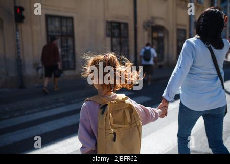 Rückansicht der Großmutter mit Enkelin, die die Straße während des Sonnenuntergangs überquert. Stockfoto