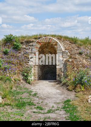 Ziegeltunnel-Eingang in der alten Festung von Komarno, Slowakei, eingebettet in einen grasbewachsenen Erdwall Stockfoto