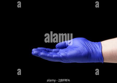 Ausgestreckte Hand in einem blauen Handschuh auf schwarzem Hintergrund, Nahaufnahme. Stockfoto