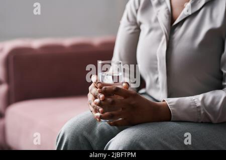 Hände einer jungen, besorgten Patientin der Counselin, die ein Glas Wasser in der Hand hielt, während sie auf der Couch saß und ihre Probleme beschrieb Stockfoto