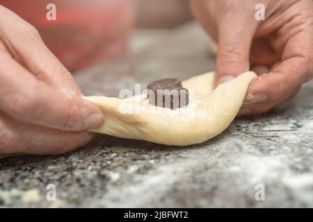 Nahaufnahme der Hände der Konditorinnen, die Schokolade in Hefeteig für Brötchen legen, selektiver Fokus Stockfoto