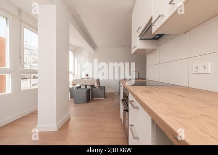Neue offene Küche mit Holzablagen, weißen Schränken und Geräten aus Edelstahl und Esstisch in einer Ecke neben einem Fenster Stockfoto