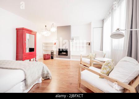 Schlafzimmer mit Doppelbett, rotem Holzschrank mit Spiegeltüren und Sesseln mit passendem Holztisch und Kamin mit Einbauregalen Stockfoto