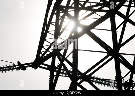 Die Sonne leuchtete hinter der Silhouette des Metallwerks eines Strompylons in Verbindung mit der natürlichen Energie der Sonne und der vom Menschen erzeugten Energie Stockfoto