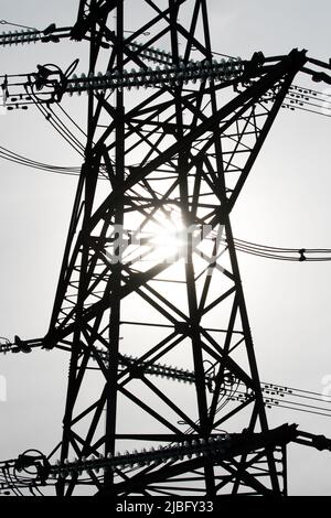 Die Sonne leuchtete hinter der Silhouette des Metallwerks eines Strompylons in Verbindung mit der natürlichen Energie der Sonne und der vom Menschen erzeugten Energie Stockfoto