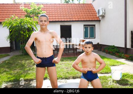 Zwei Brüder, die während ihrer Sommerpause mit Wasser spielen, um die Muskeln spielen und herumspielen Stockfoto