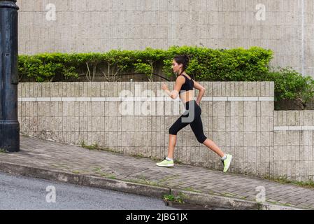 Schlanke junge Frau, die auf dem Bürgersteig der Stadtstraße bergauf läuft. Weibliche Sportlerin, die draußen trainiert. Stockfoto