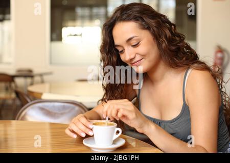 Lässige glückliche Frau, die Kaffee rührt, sitzt in einem Restaurant Stockfoto