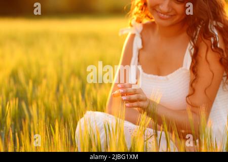 Glückliche Frau, die bei Sonnenuntergang auf einem Feld Weizen berührt Stockfoto