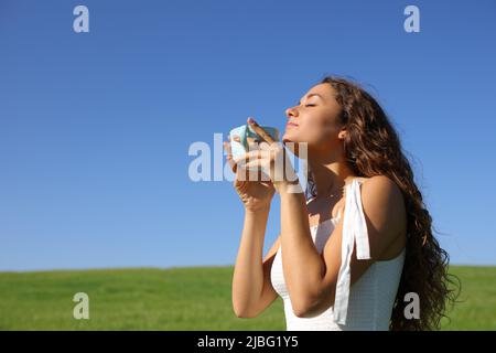 Frau riecht Kaffeetasse auf einem grünen Feld ein sonniger Tag Stockfoto