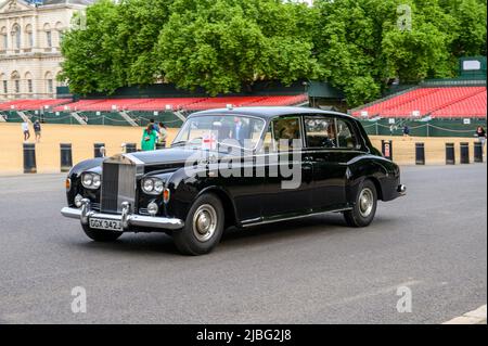 LONDON - 18. Mai 2022: Chauffeur-gesteuerter Classic Rolls Royce mit englischer Flagge passiert die Horse Guards Parade mit gut gekleideten Passagieren Stockfoto