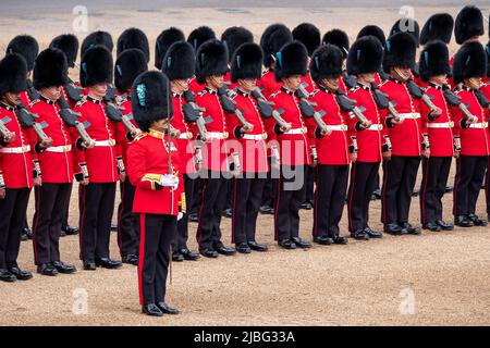 Wachen und Frauen in schwarz-roten Uniformen marschieren bei Horseguards, Westminster London UK, während der Trooping the Colour Militärparade. Stockfoto