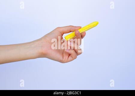 Hand hält Kreide auf isoliertem weißem Hintergrund. Frau, die etwas mit gelber Kreide schreibt. Stockfoto