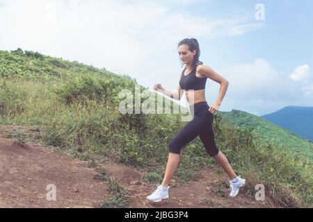 Langlaufloipe für Frauen, die im Sommer auf dem Bergpfad läuft. Frau in schwarzer Sportkleidung, die in der wilden Natur im Freien trainiert. Stockfoto