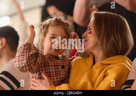 Begeisterte Fußballfans, Mutter mit kleiner Tochter, die die deutsche Nationalmannschaft in einem Live-Fußballspiel im Stadion unternahmen. Stockfoto