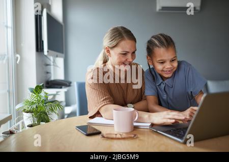Porträt einer multiethnischen Familie, glücklicher Mutter und Tochter, die beim gemeinsamen Lernen zu Hause auf den Laptop-Bildschirm blicken und Platz kopieren Stockfoto