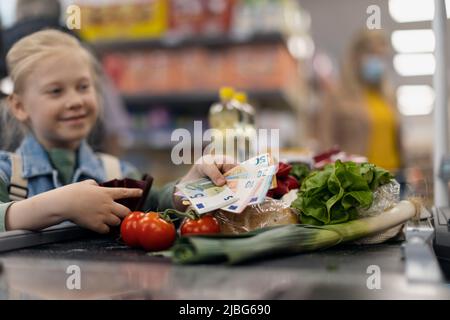 Nahaufnahme eines kleinen blonden Mädchens, das für den Einkauf im Supermarkt bezahlt. Stockfoto