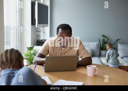 Porträt von Schwarz Bleiben Sie zu Hause Vater mit Laptop mit zwei Kindern im Hintergrund, Platz zum Kopieren Stockfoto