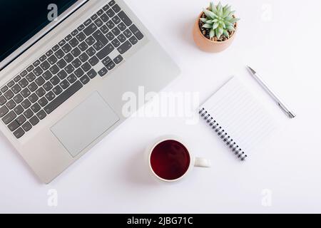 Weißer Arbeitsplatz mit Laptop, Tasse Tee, Notizblock und Sukculent. Home Office, Geschäftskonzept. Draufsicht, flach liegend. Stockfoto