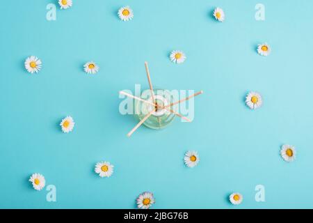 Glasflasche mit Aroma-Diffusor und Gänseblümchen auf hellblauem Hintergrund. Sommerkonzept. Draufsicht, flach liegend. Stockfoto