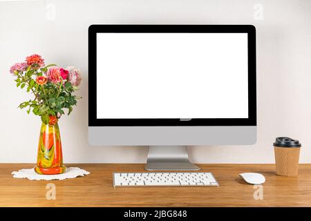Leerer Bildschirm-Desktop-Computer mit drahtloser Tastatur und Maus auf einem Holztisch in einem Arbeitszimmer mit einer Vase mit Rosenblüten und einer tasse kaffee von peper Stockfoto