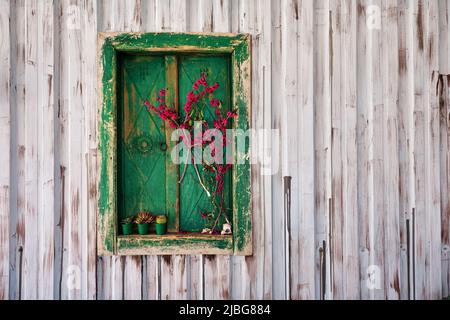 Grüner hölzerner antiker Fensterrahmen mit Fensterläden und verziert mit Blumen auf Stahlwandplatte. Stockfoto