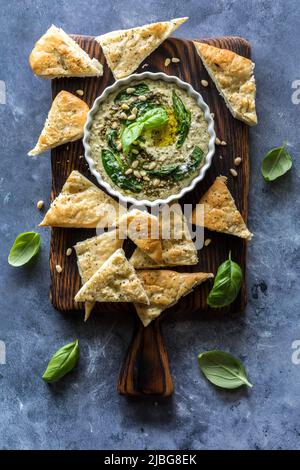 Draufsicht auf einen Pesto-Hummus, der von dreieckigen Pitabips umgeben ist. Stockfoto