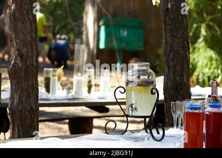 Hochzeitsfeier Bankett im Freien im Wald. Esstisch im Boho-Stil mit Kerzen, weißem Tuch, Blumen, serviert mit Tellern, Geschirr dekoriert Stockfoto