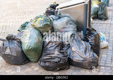 Mehrere Plastiksäcke mit Müll neben dem Behälter. Das Problem der Reinigung in Städten Stockfoto
