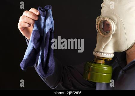 Ein Mann in einer Gasmaske hält schmutzig riechende Socken. Das Problem des unangenehmen Fußgeruchs bei Männern Stockfoto