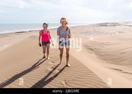 Frontalansicht von zwei Frauen, die auf einer großen Düne laufen. Mutter und Tochter Stockfoto