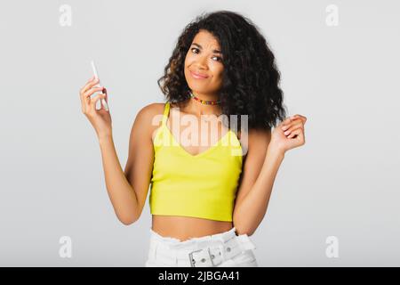Unzufrieden afroamerikanische Frau hält Smartphone isoliert auf grau Stockfoto