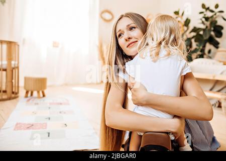 Junge Mutter umarmt und küsst ihre kleine Tochter Stockfoto