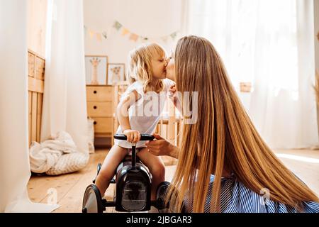 Junge Mutter umarmt und küsst ihre kleine Tochter Stockfoto